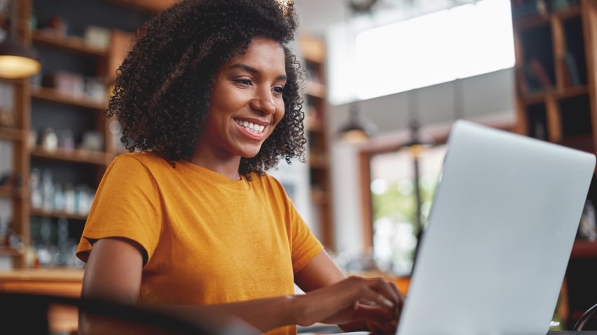 Look up the Name in the Search Results A smiling woman in an orange t-shirt working on her laptop.
