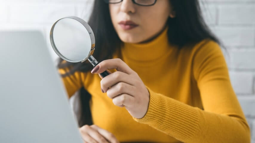 4 TikTok SEO Ranking Factors A woman holding a magnifying glass to her laptop screen while researching TikTok SEO ranking factors.