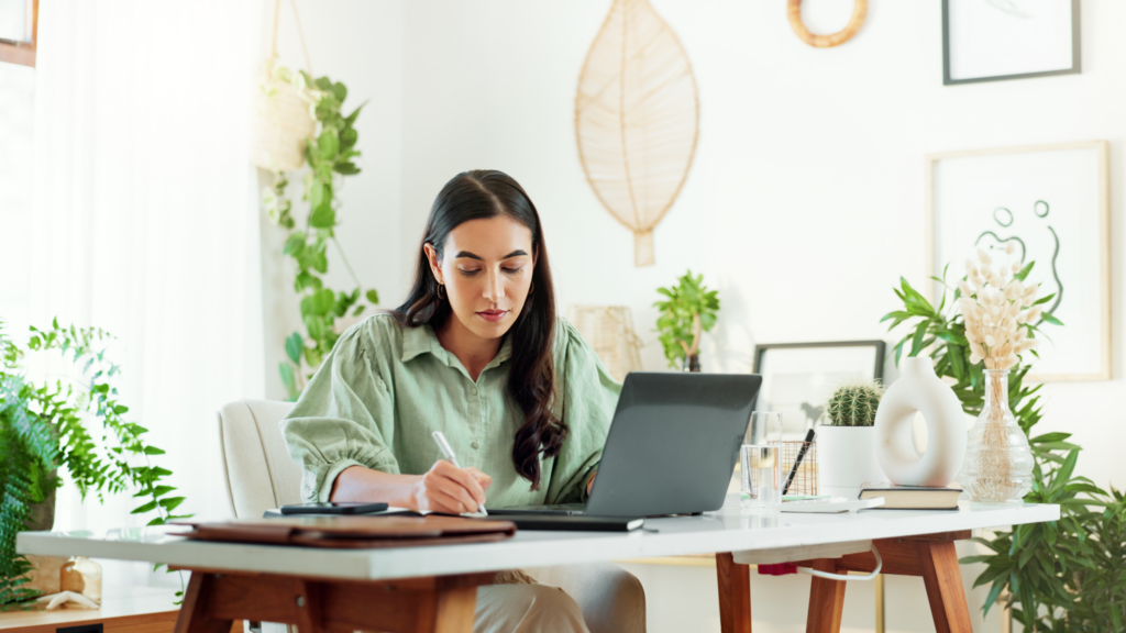 Offer social media managment services A woman smiles while seated at a table, working on social media management.
